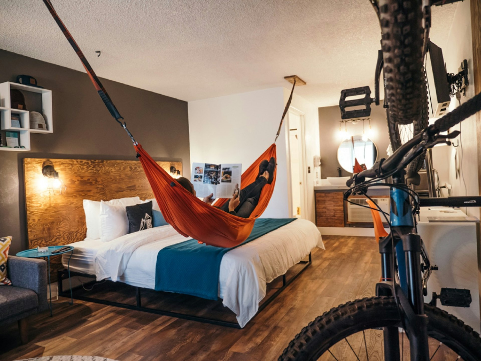 A trendy hotel room with bikes hanging on the wall and a person reclining in a hammock from the ceiling