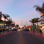 An empty street lined with palm trees with an arch at one end under a blue sky dotted with pink clouds