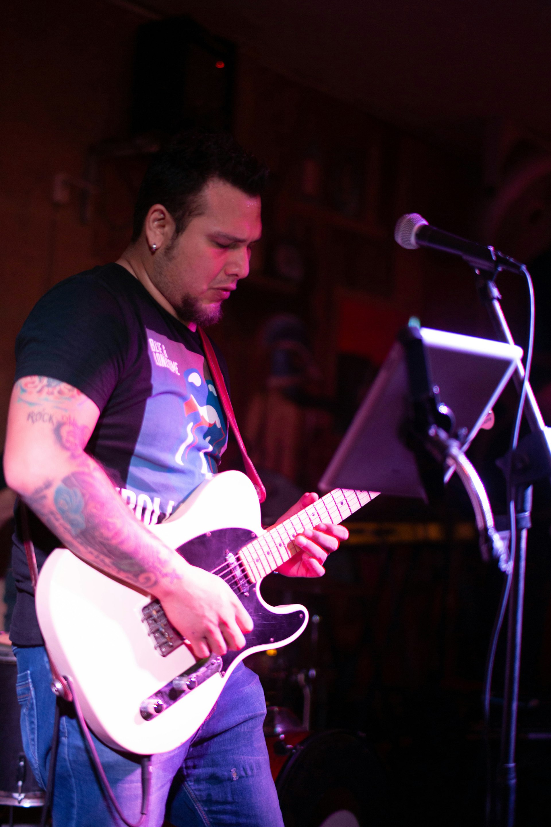 A man in a t-shirt plays the guitar with a microphone in front of him