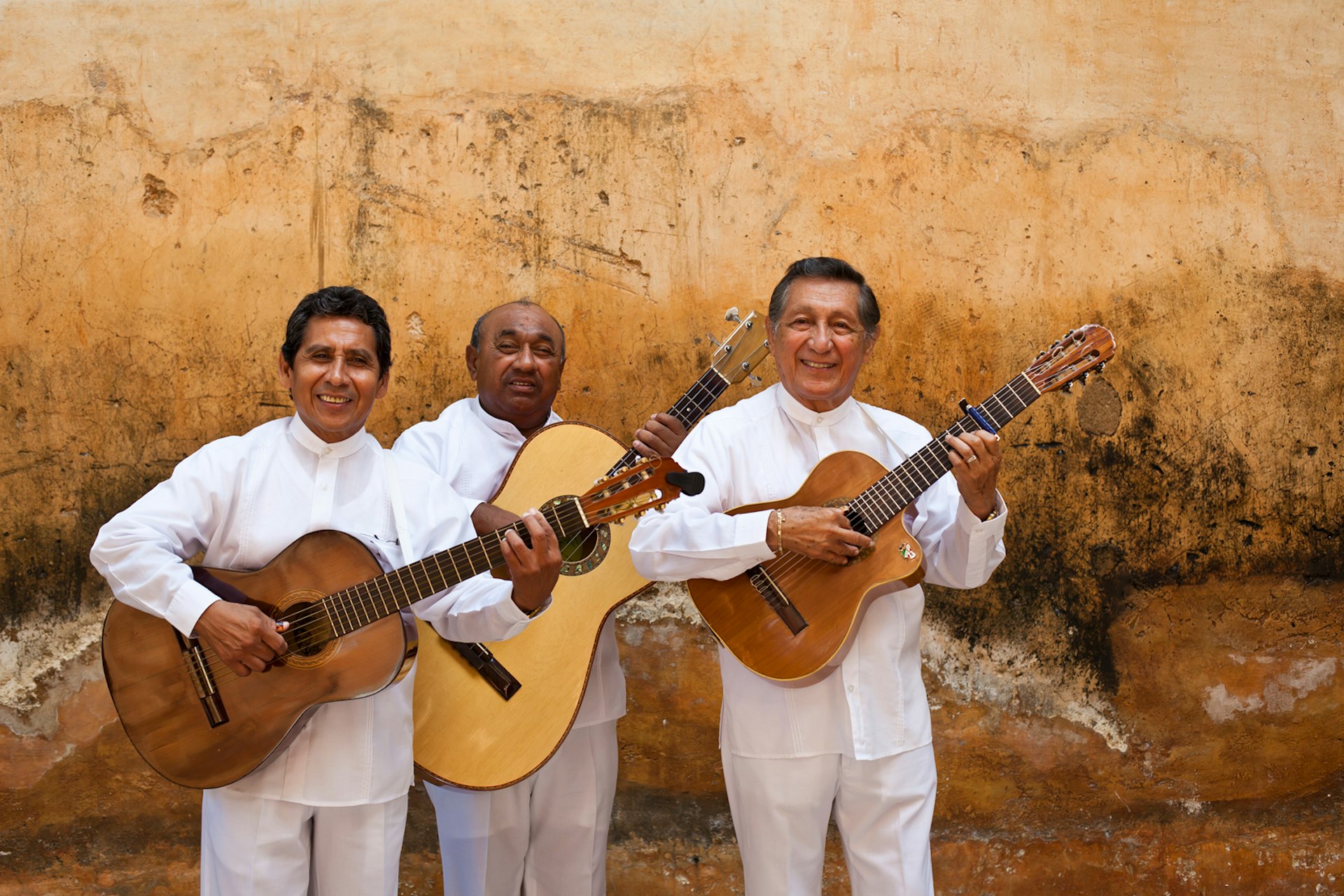 Three men in white outfits hold string instruments 