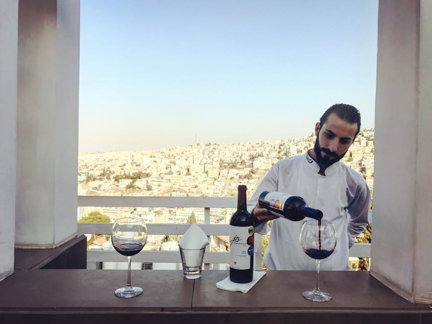 Bartender pours a glass of local Jordan River Shiraz with a view of Amman from Cantaloupe's upper terrace