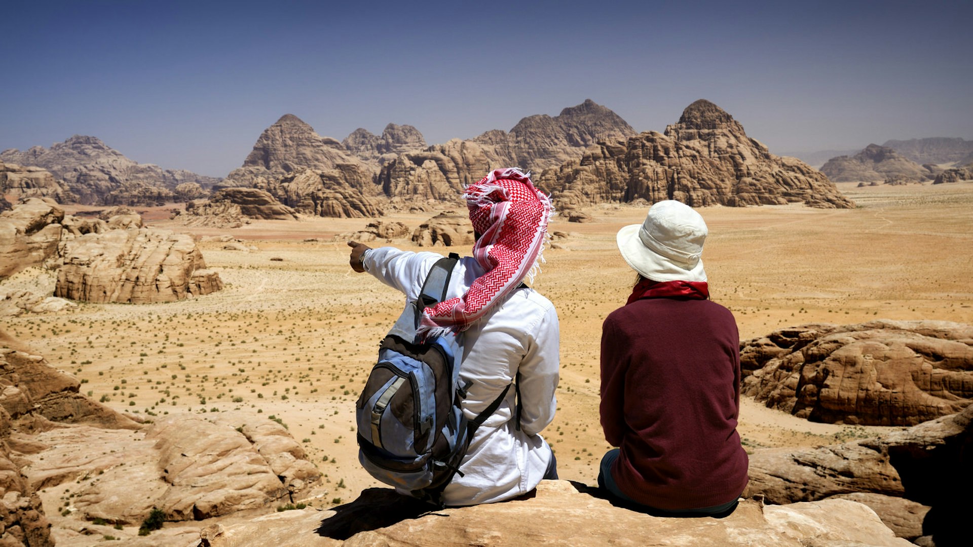 Tourist and local Bedouin guide sit on a rock in Wadi Rum, Jordan, contemplating the landscape from the mount Jebel Burdah