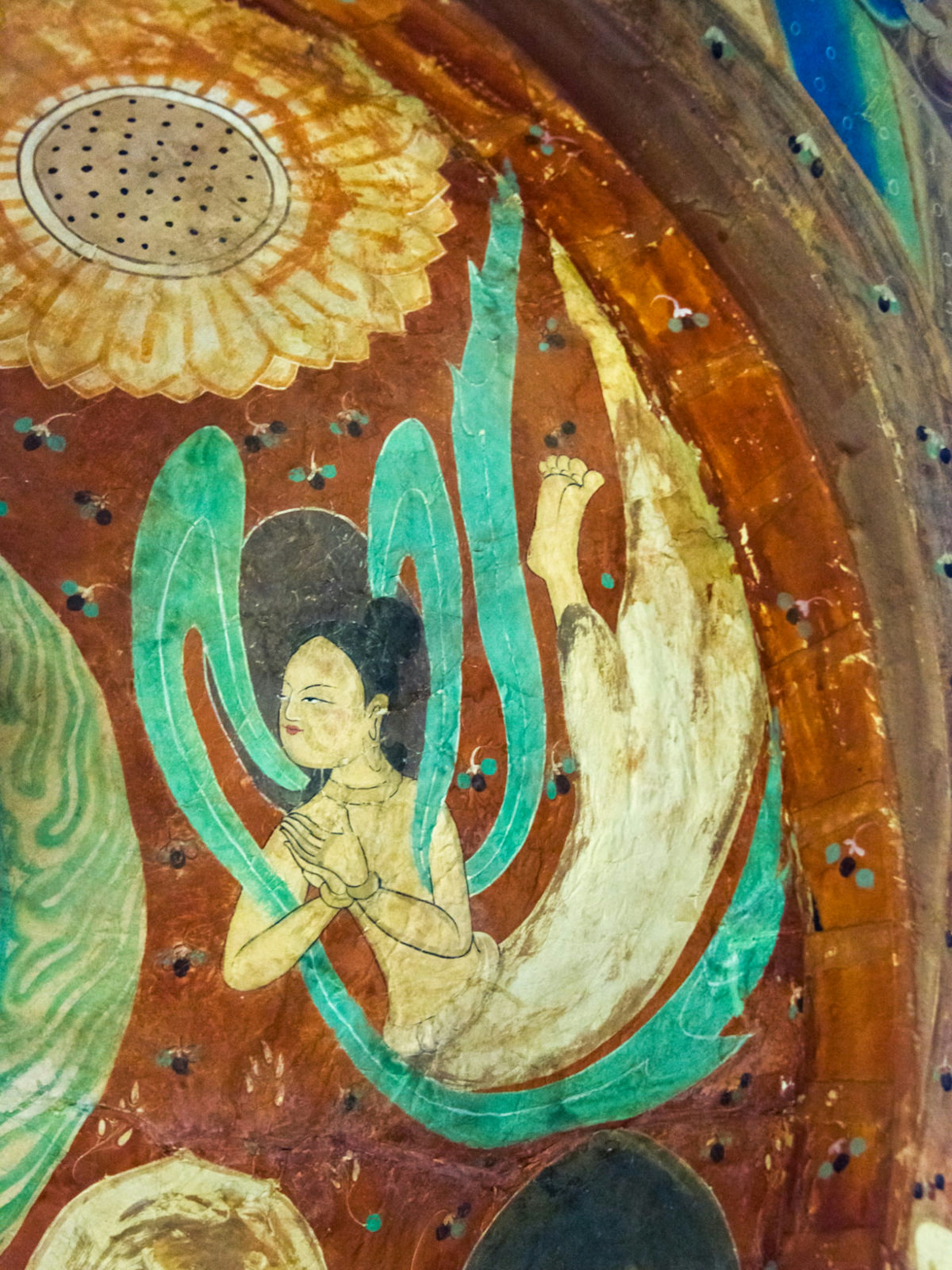 A mural of a flying Buddhist being with black hair and wafting green robes