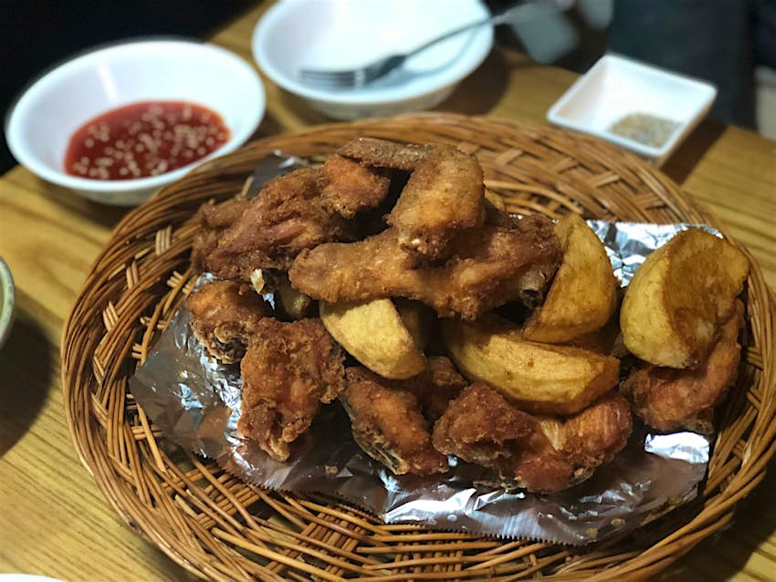 A basket of Korean fried chicken and potato wedges with accompany dish of red dipping sauce