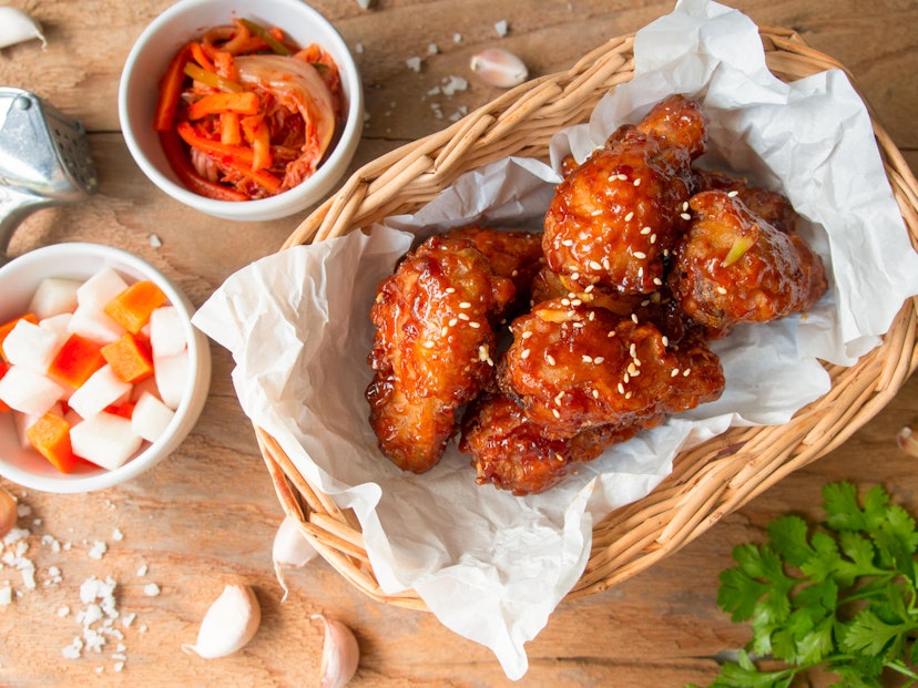 A basket of Korean fried chicken with sides of pickled radish and cloves of garlic on a wooden table