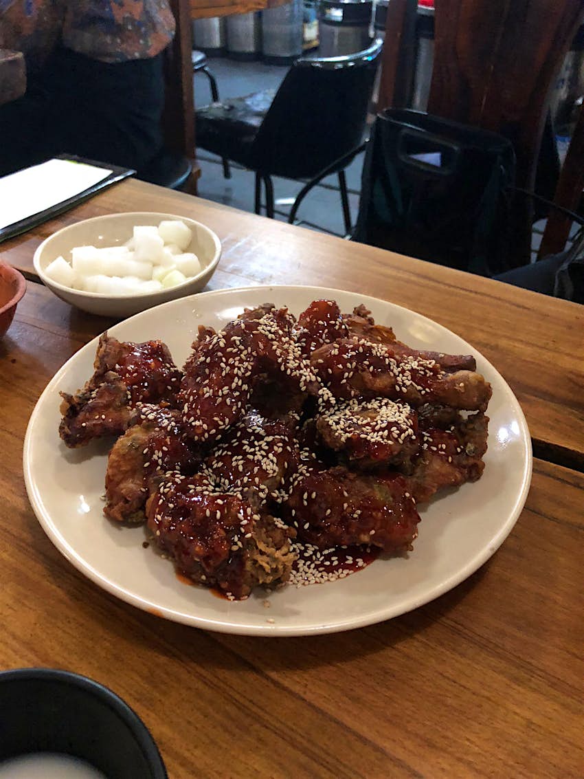 A plate of marinated Korean fried chicken covered in sesame seeds on a wooden table