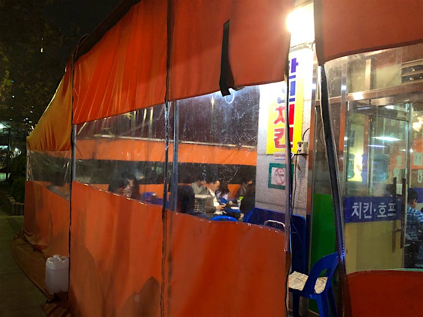 An orange tent with windows looking in to diners and an illuminated sign in Korean script