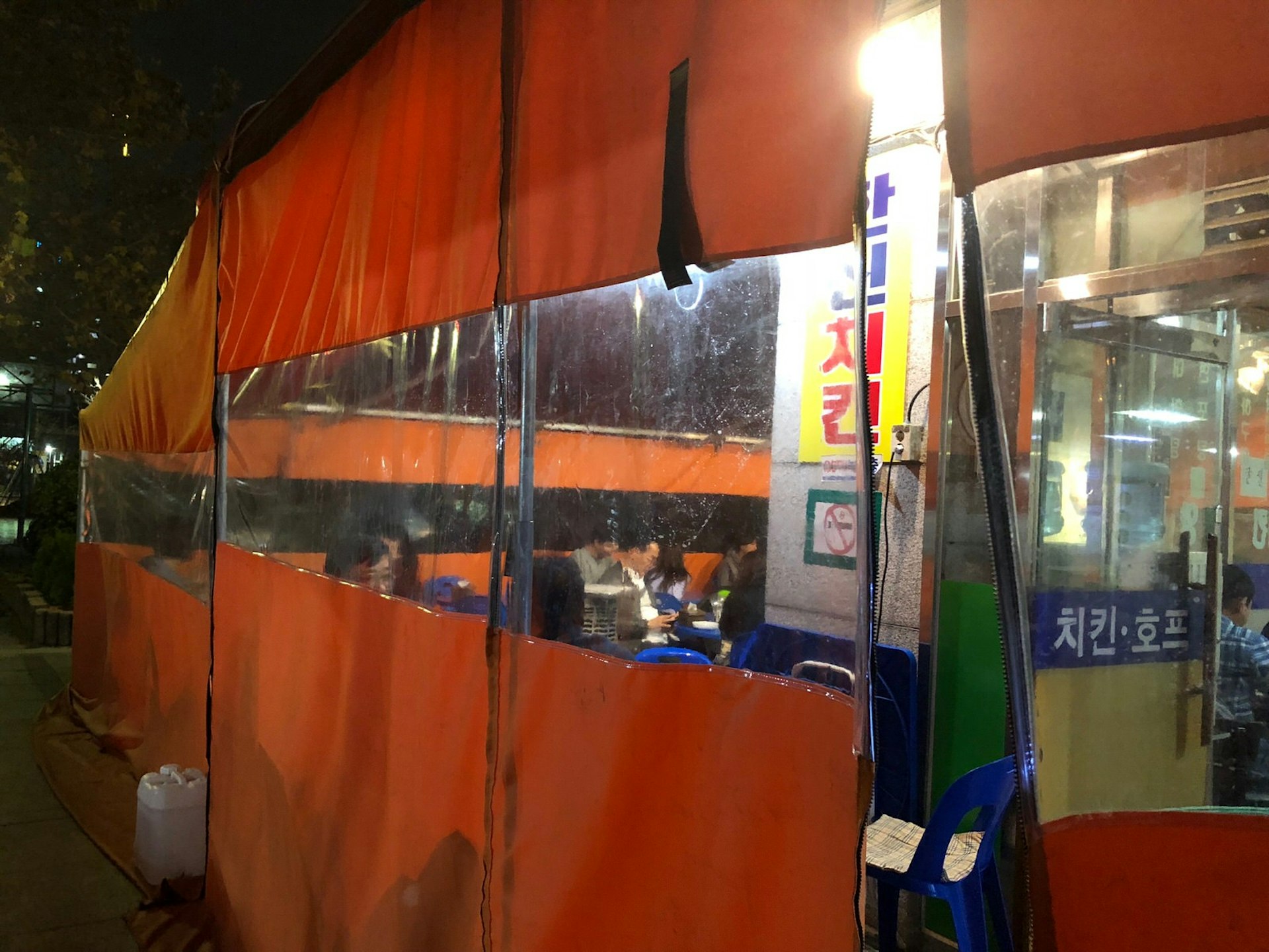 An orange tent with windows looking in to diners and an illuminated sign in Korean script