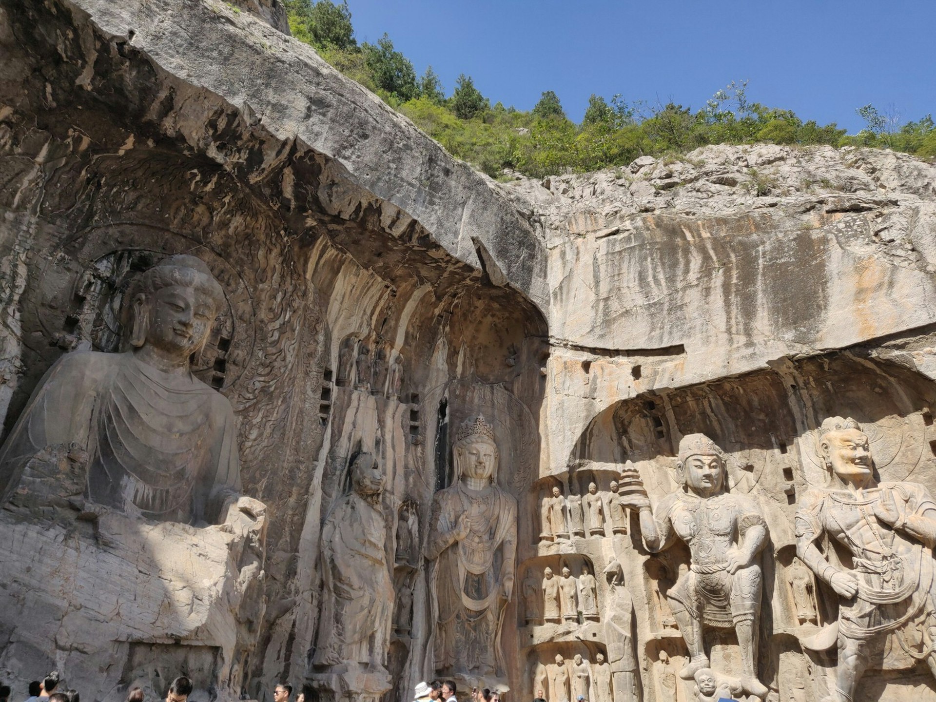 5 ornate Buddhas and guardians are carved into a grey stone cliffside cave