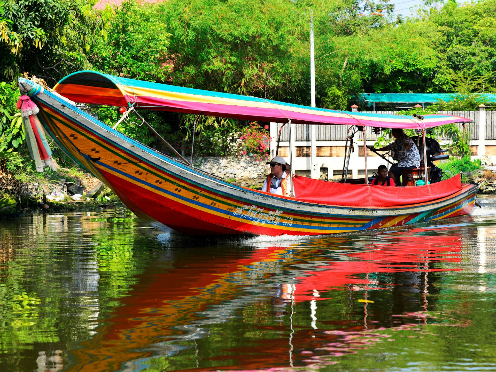 A colourful longtail boat with passengers on one of Bangkok's waterways backed by greenery.