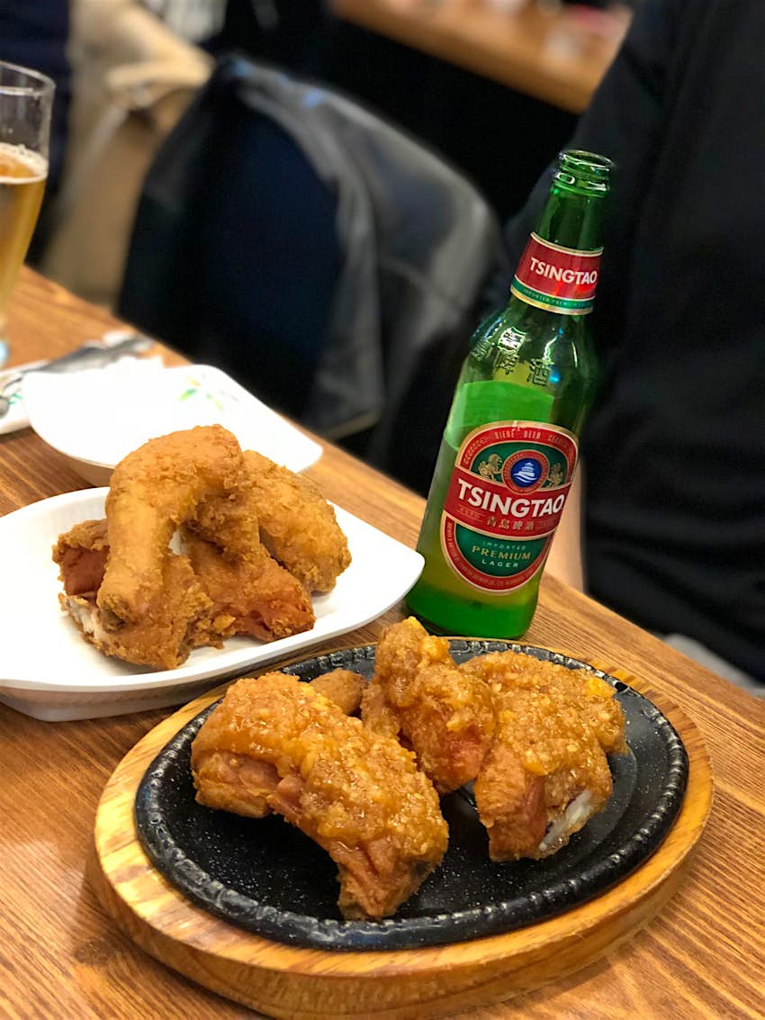 Chicken on a black sizzling platter next to a bottle of Tsingtao beer on a wooden table