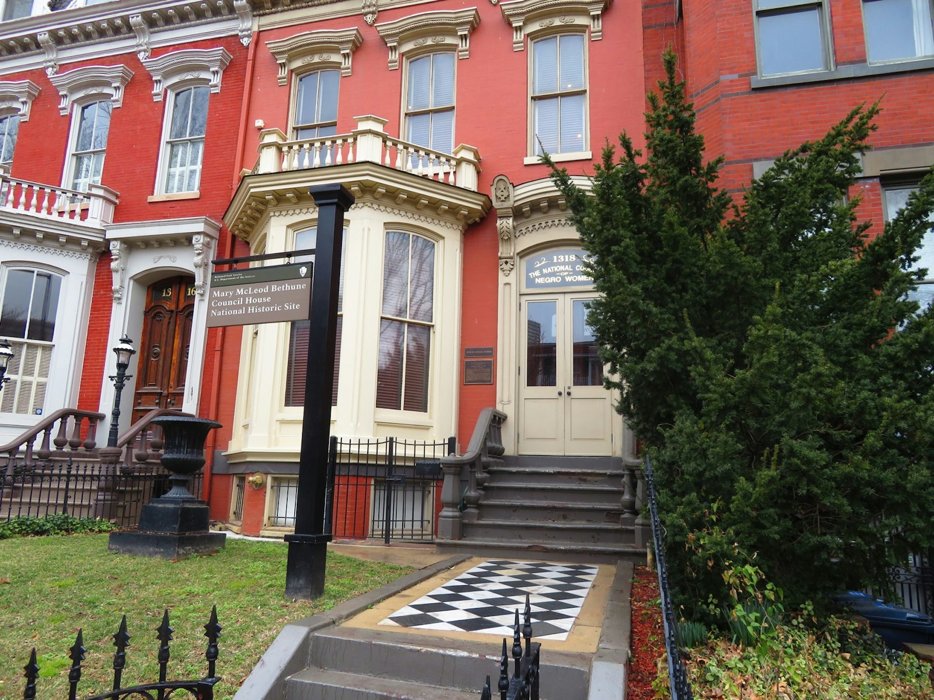 A checkerboard patterned walkway leads to a red row house with a cream-colored dormer window