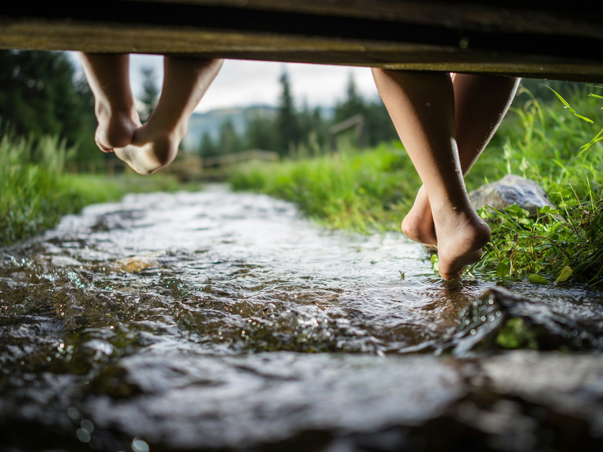 Two children sitting on a bridge, dipping their feet in a river