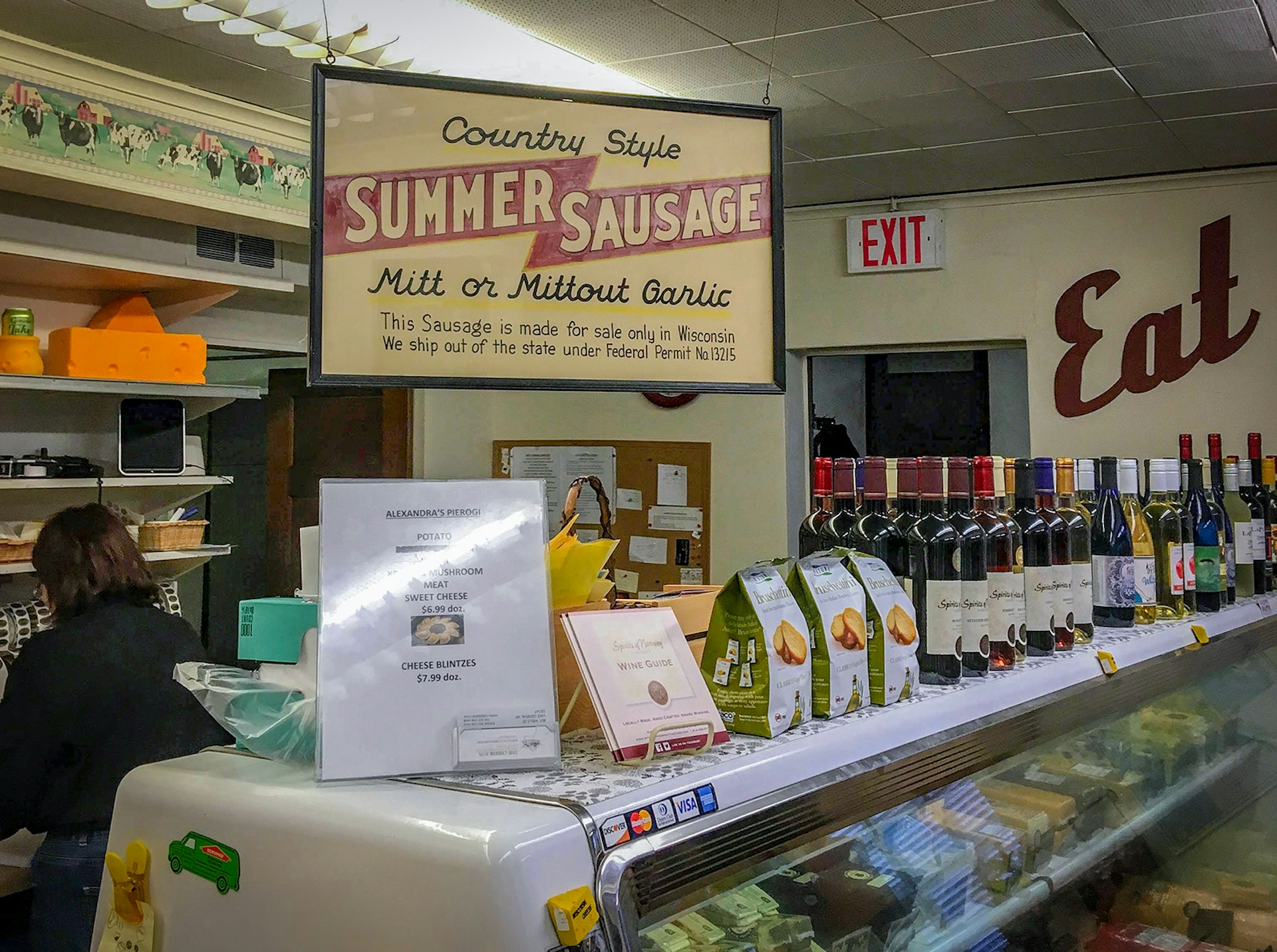 A deli counter lined with wine bottles underneath a sign advertising summer sausage in Geneva Lake, Wisconsin