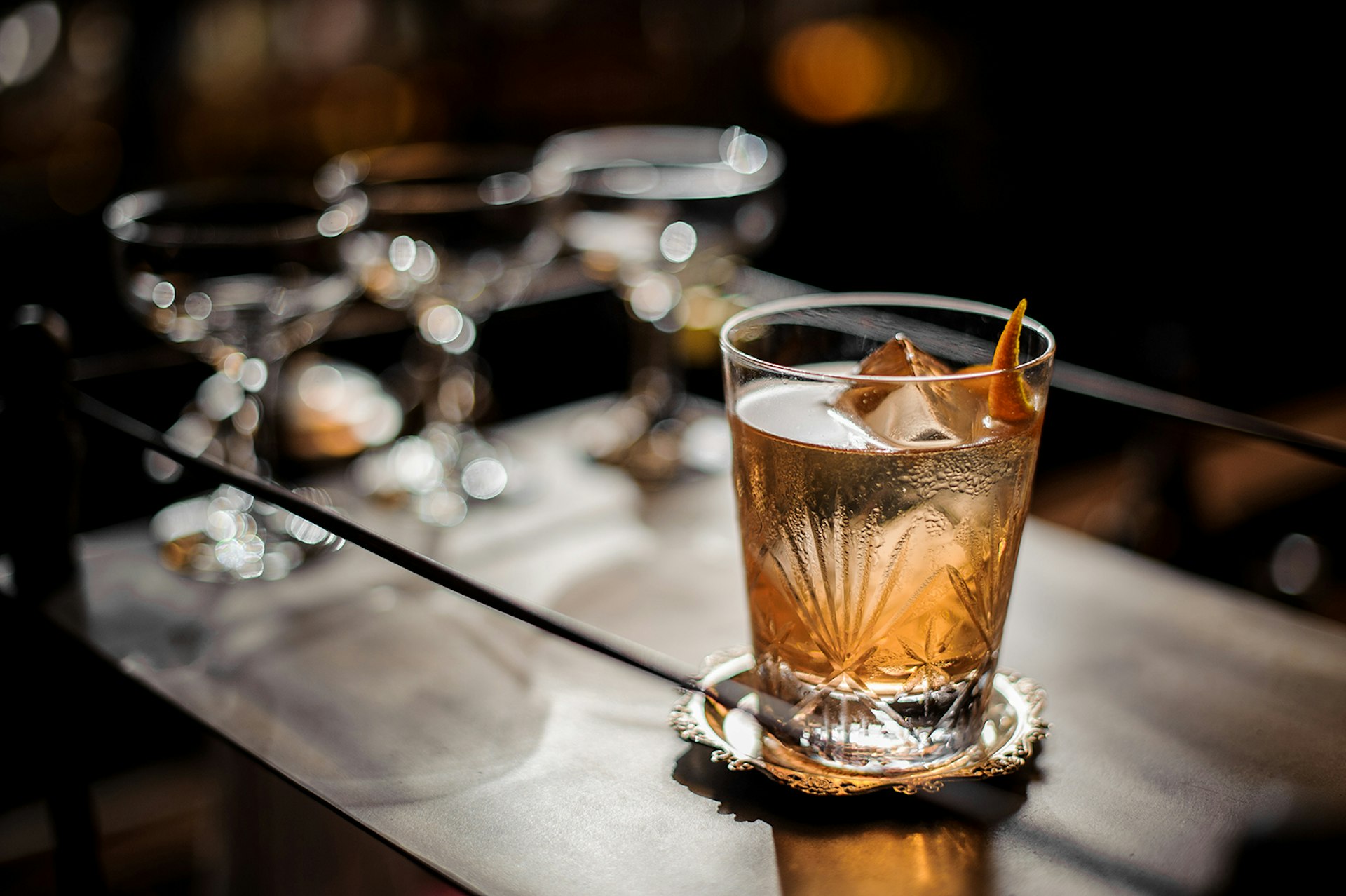 An old fashioned cocktail sits on the dark wood of a bar cart