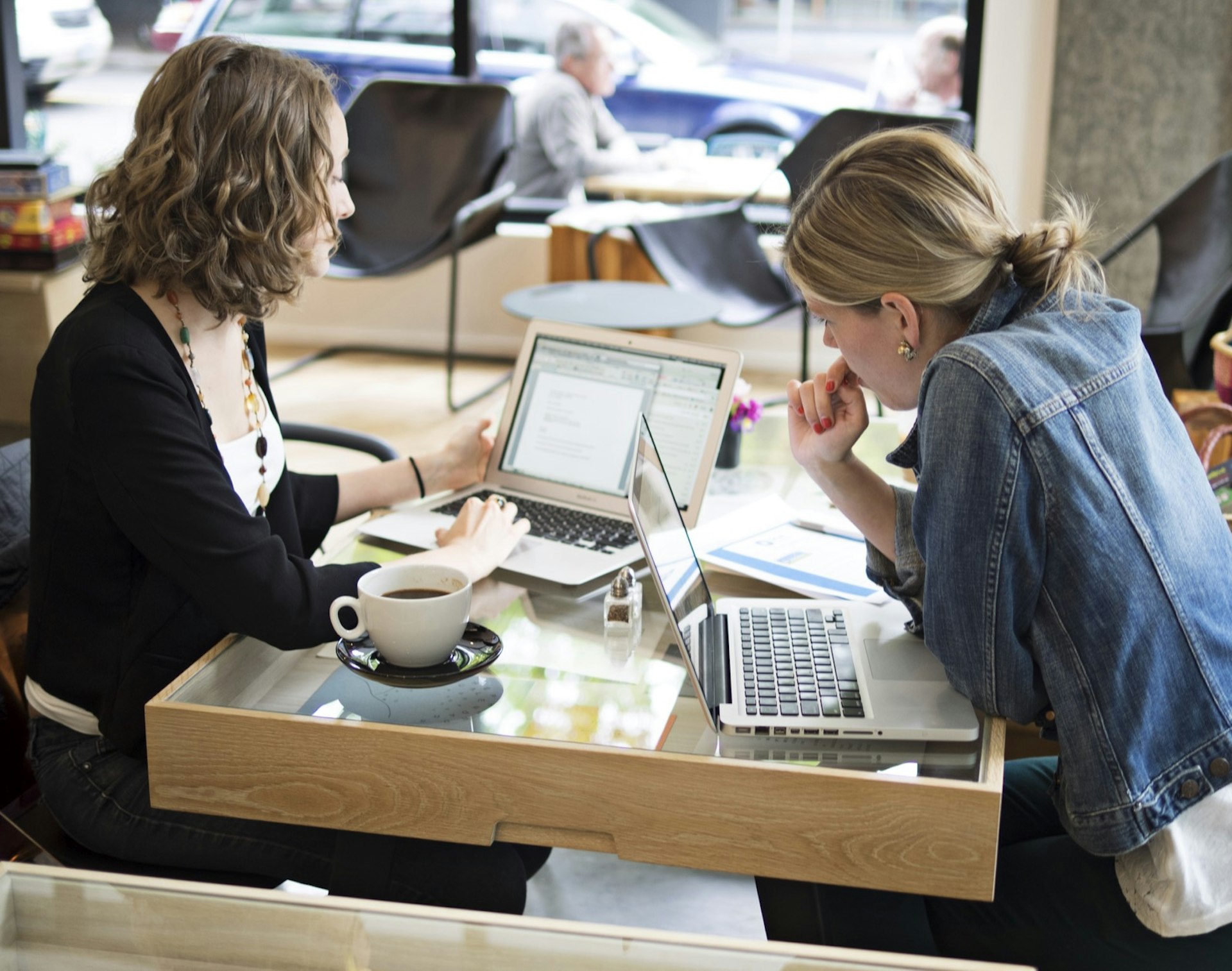 Two women sit at a cafe in Portland with coffee and laptops open.