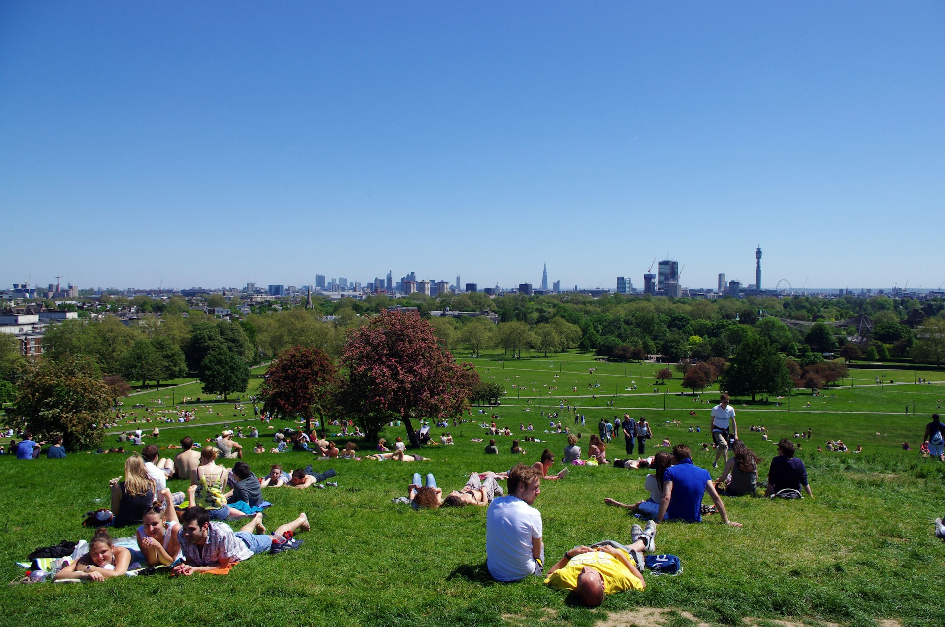 People sitting on Primrose Hill in the summer sun with London in the background