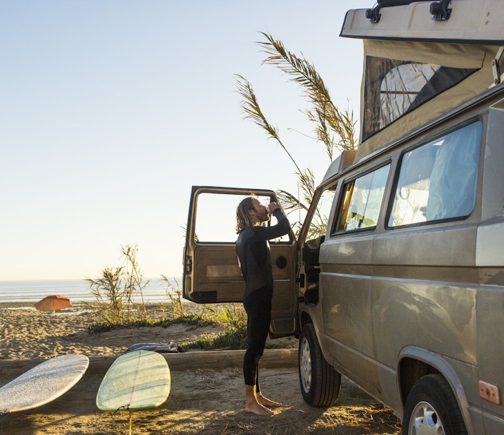 Features - Side view of male surfer having drink outside mini van on San Onofre State Beach
