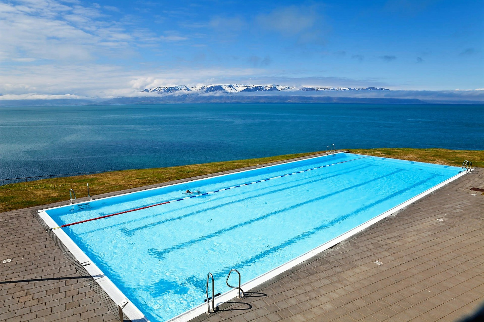 Outdoor swimming pool on the side of a fjord with mountains in the distance