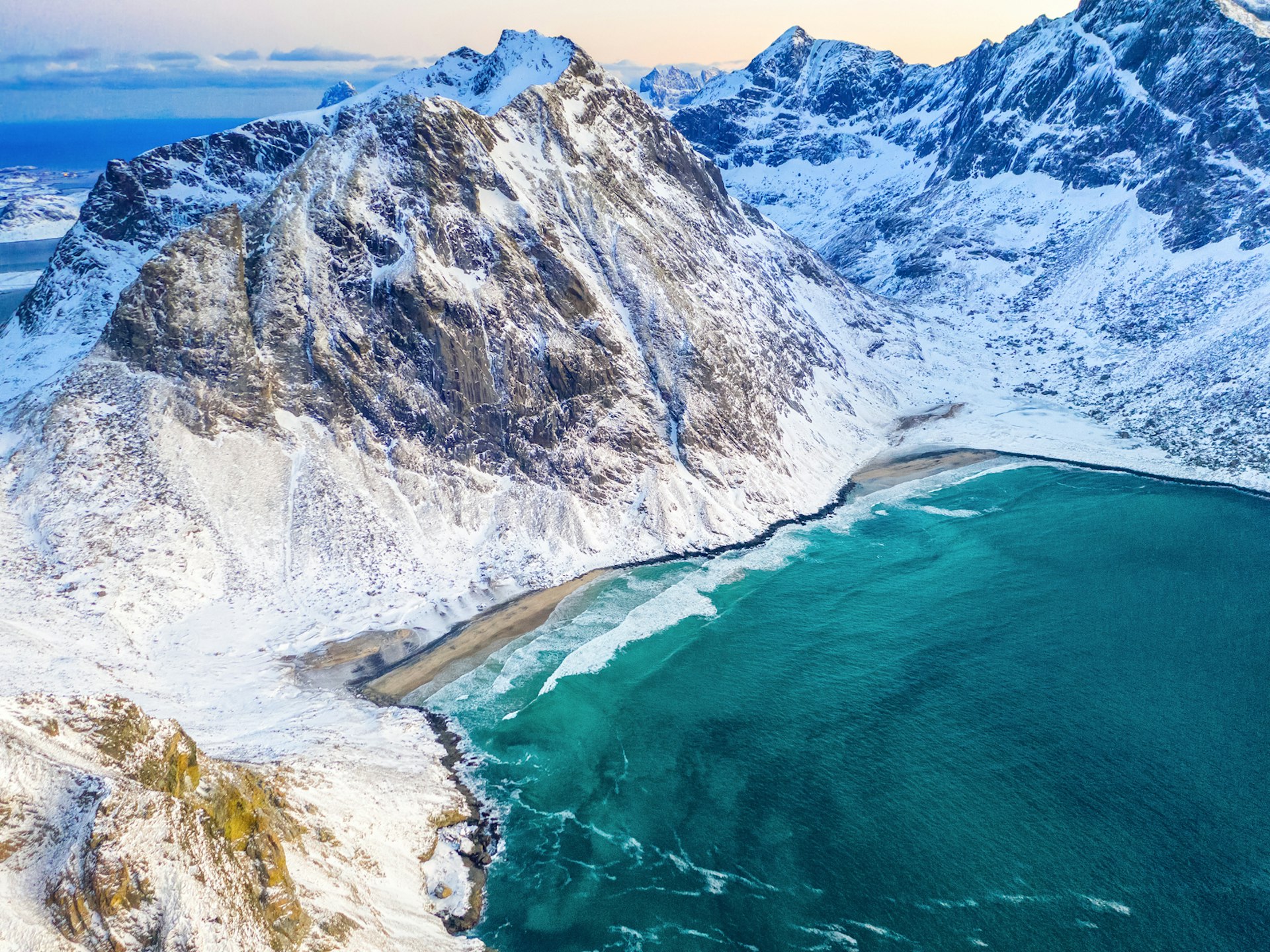 An aerial shot over the snowy mountains and bright-blue waters of Kvalvika Beach