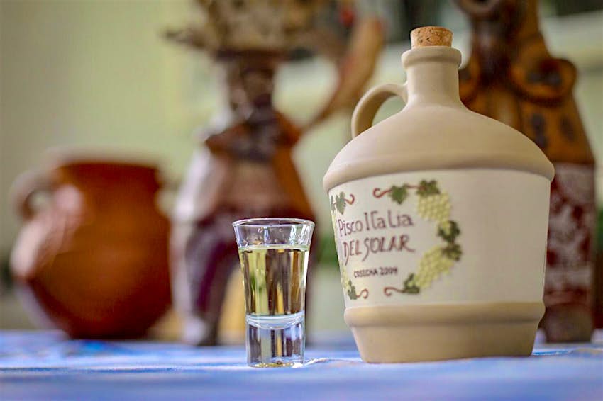 A close up of a small glass of pisco next to a clay jar closed with a cork in Lima, Peru
