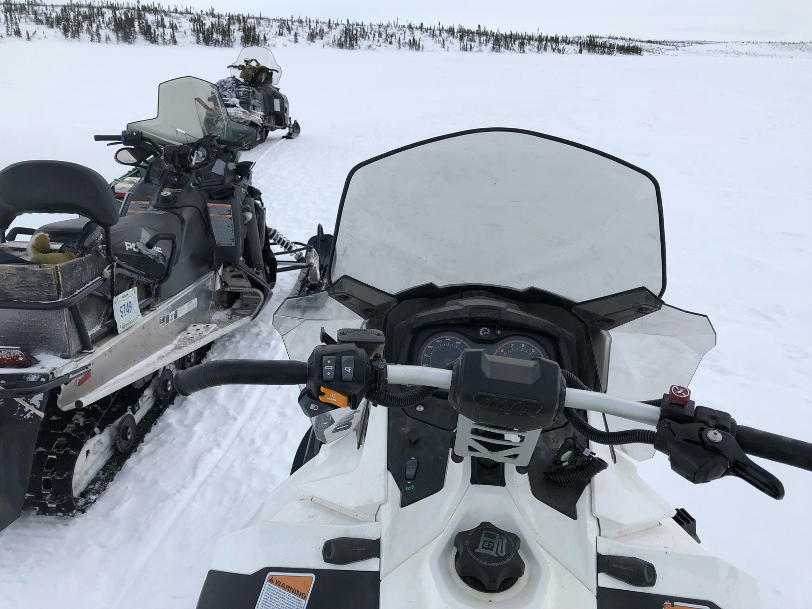 Looking down on a white snowmobile from the saddle, with a line of trees ahead in the Northwest Territories