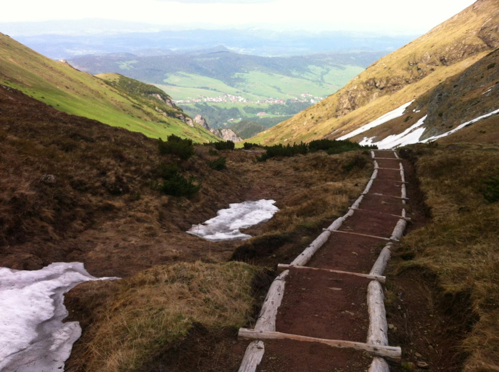 A basic path made from logs and soil snakes down the hillside, with a view of the lush valley in the distance