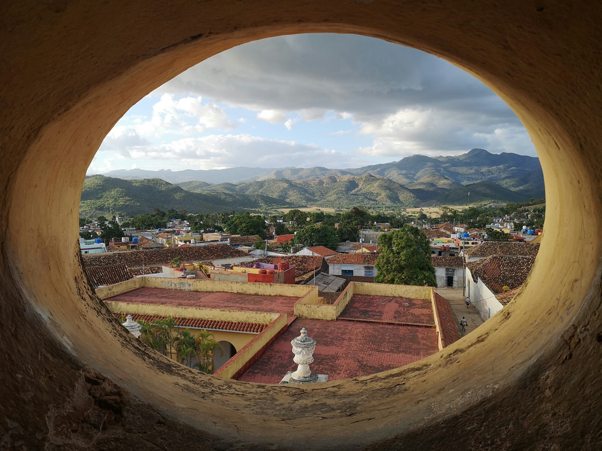 The red tiled-roofs of homes in Trinidad, Cuba, with a series of green mountains in the background 