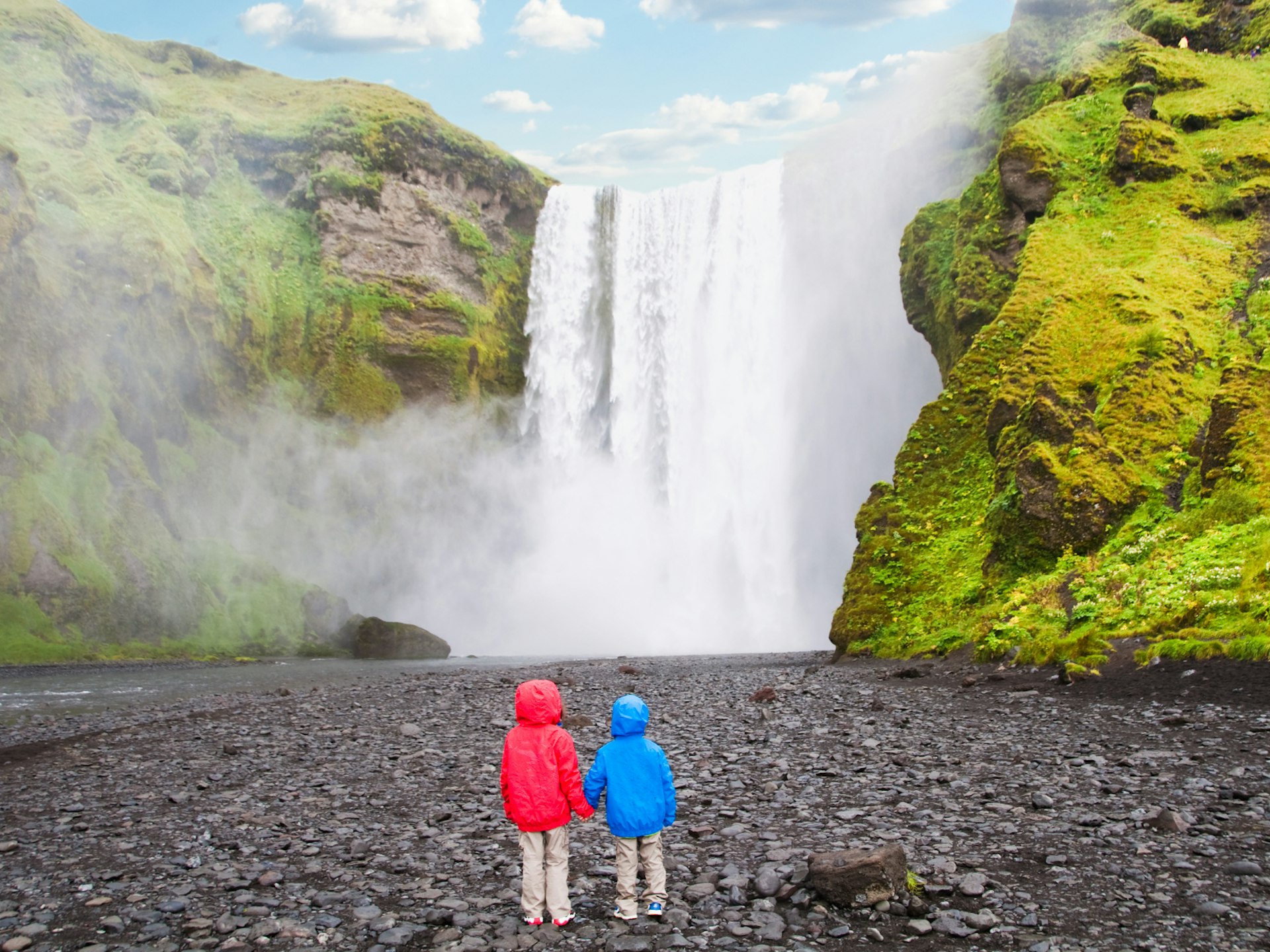 Two children looking at majestic Skogafoss waterfall in Iceland