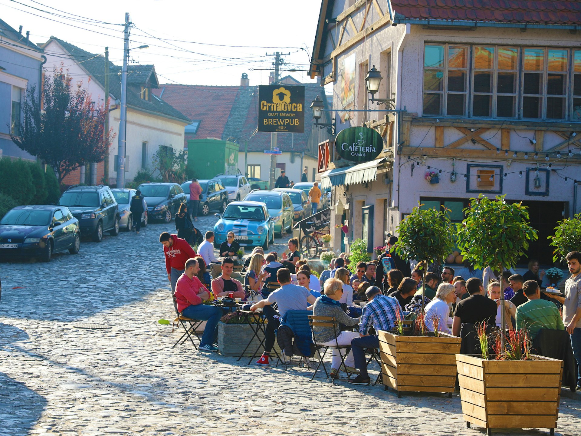 People sitting outside in front of a pub on a cobblestoned street in Zemun