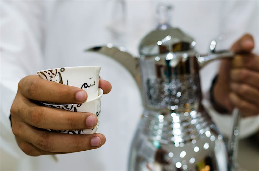 A man pours Arabic coffee from a silver dallah