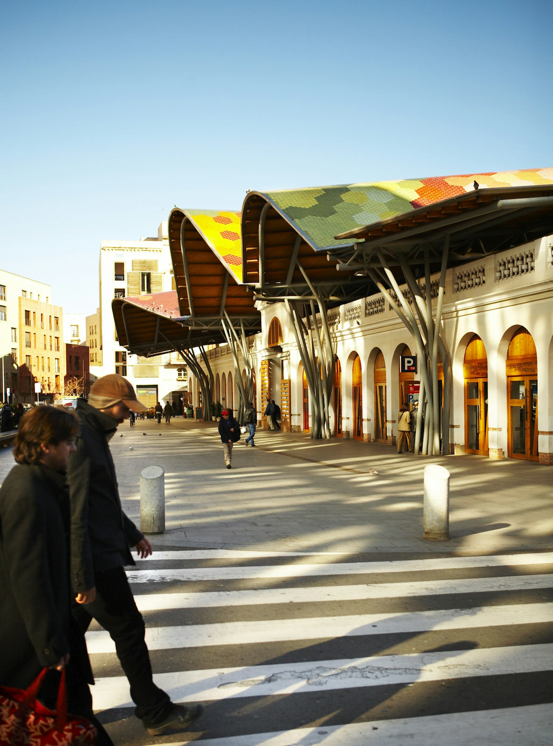 Shoppers walking past a large market hall building with a multi-coloured undulating roof