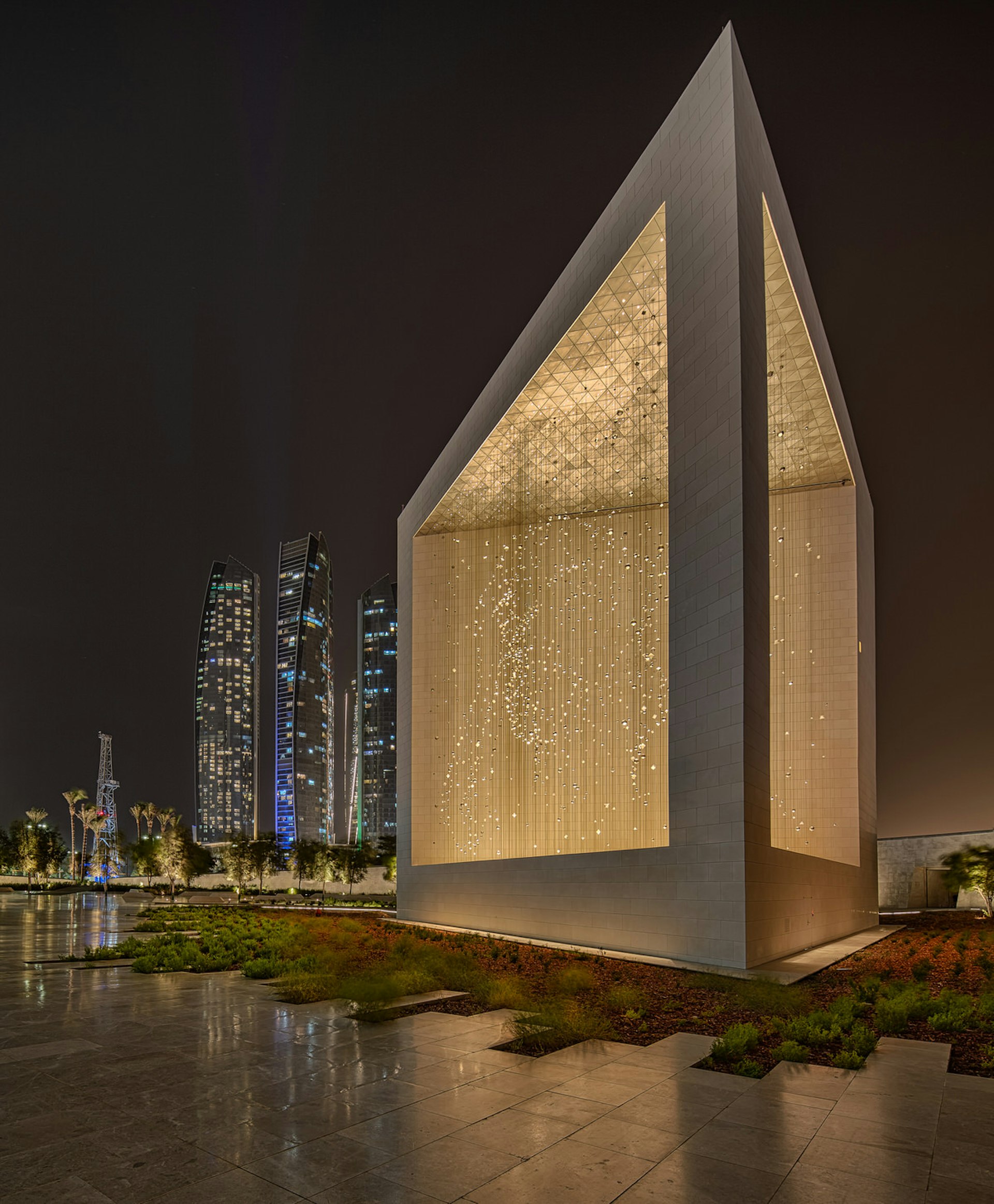 The iconic Founder's Memorial is lit up in front of a row of skyscrapers in Abu Dhabi, United Arab Emirates