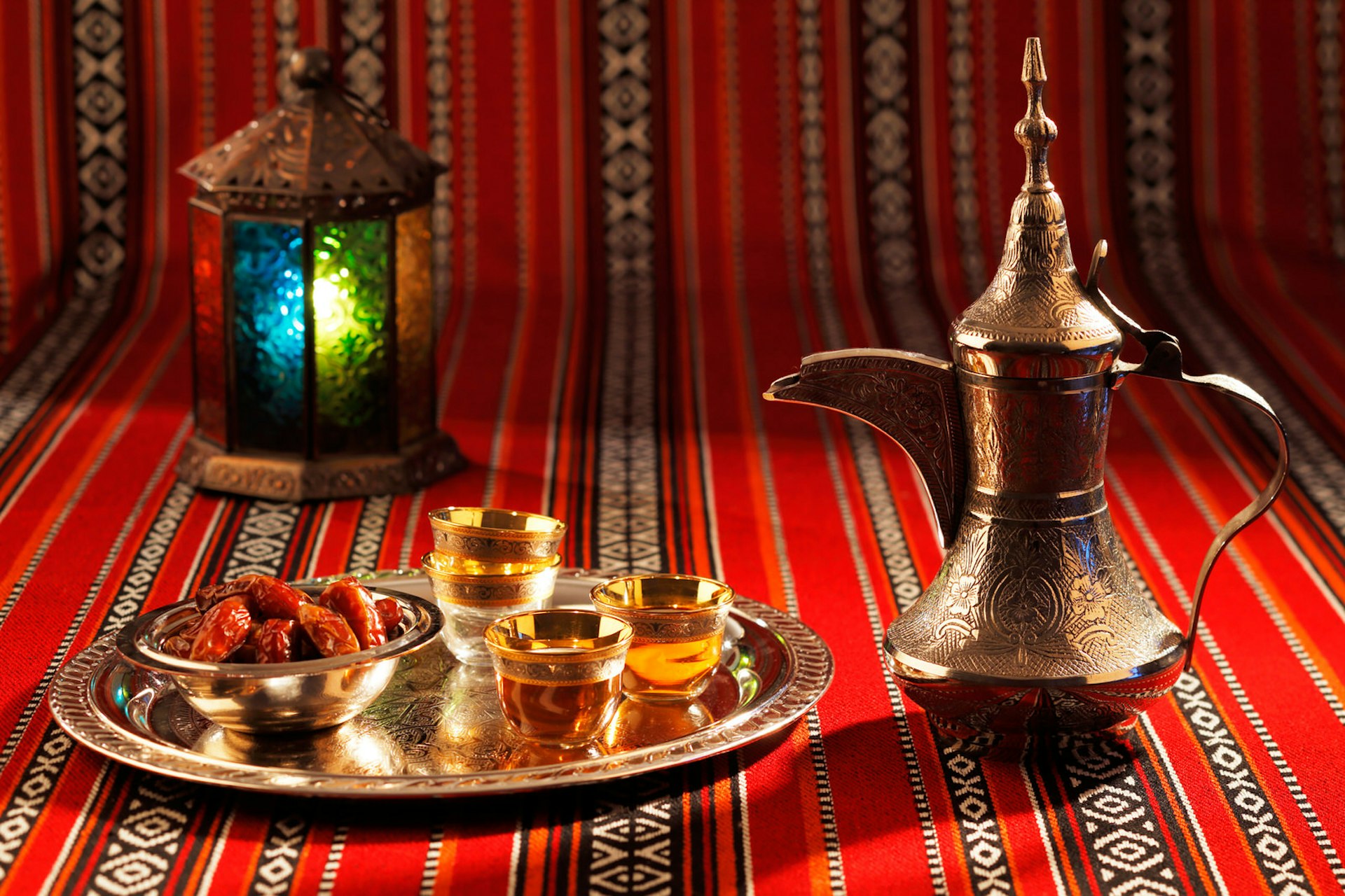 A bowl of dates and a traditional dallah coffee pot sit on Arabian-style fabric