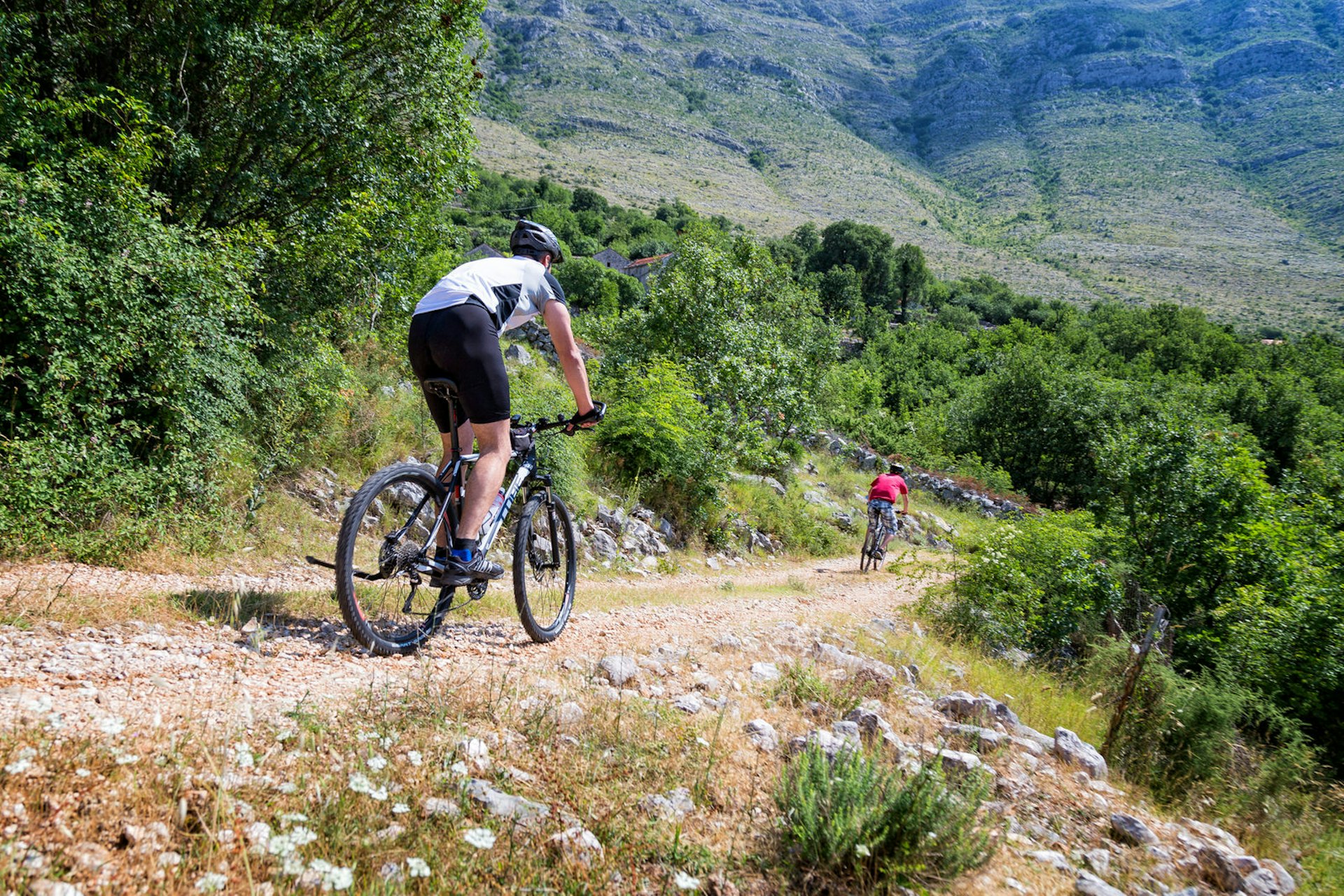 Two men on mountain bikes descend down a steep rocky path