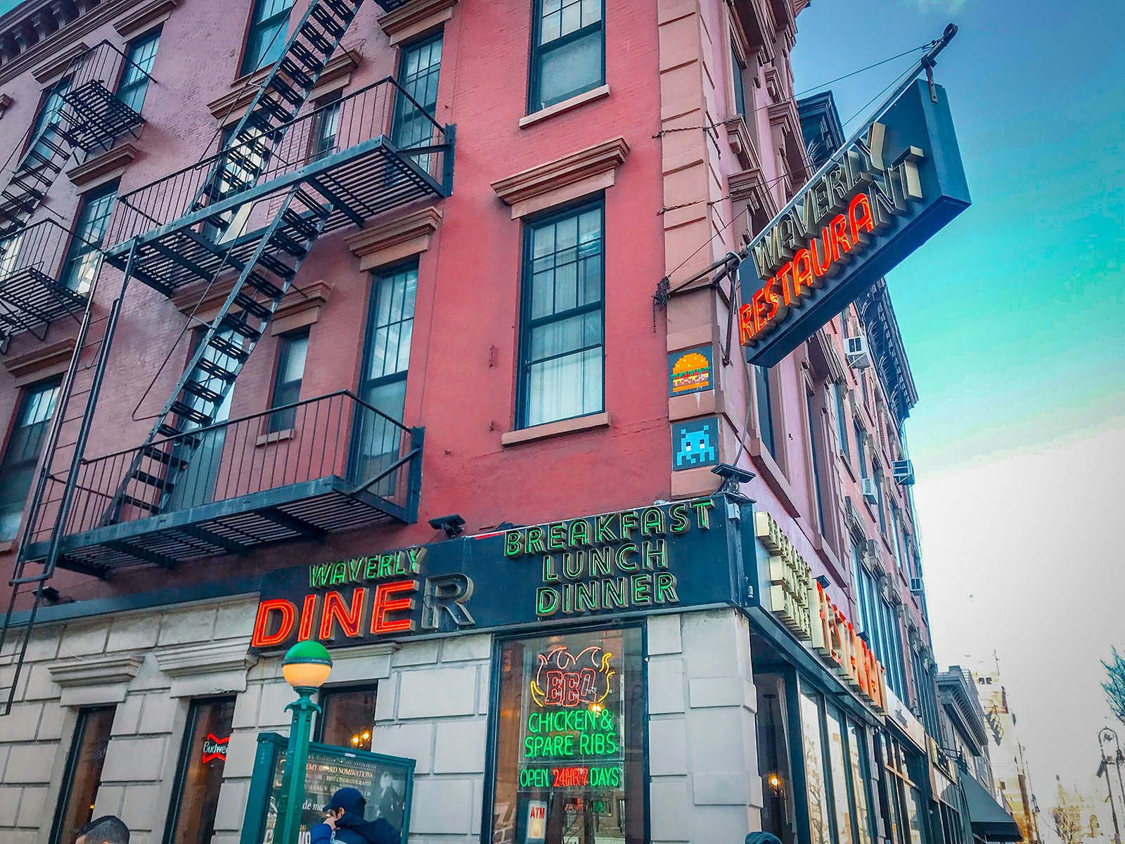 A photo of a diner on a corner in New York City, with neon signs and fire-escapes visible. 