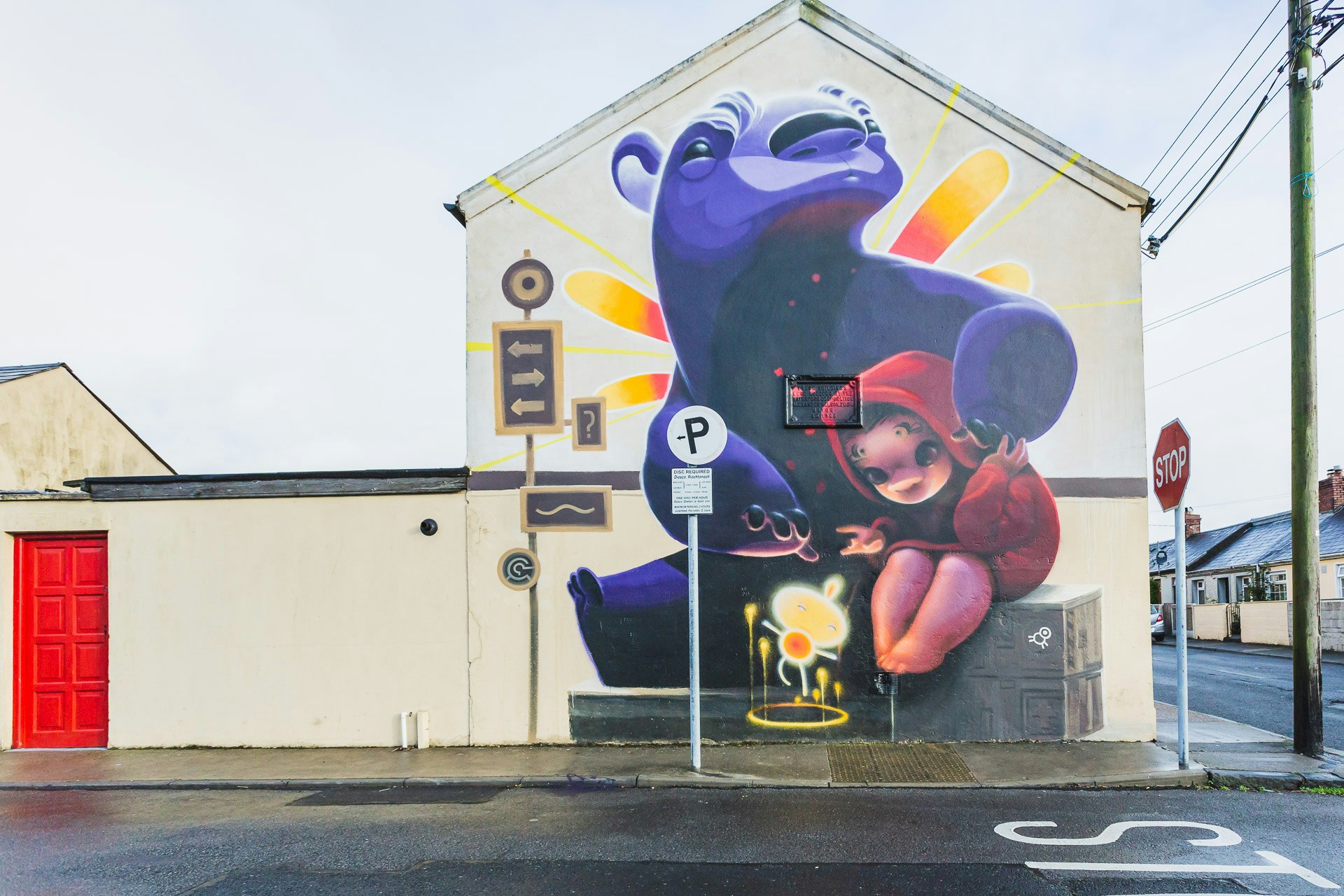 A street art mural of a purple bear hugging a small girl in a red jacket.