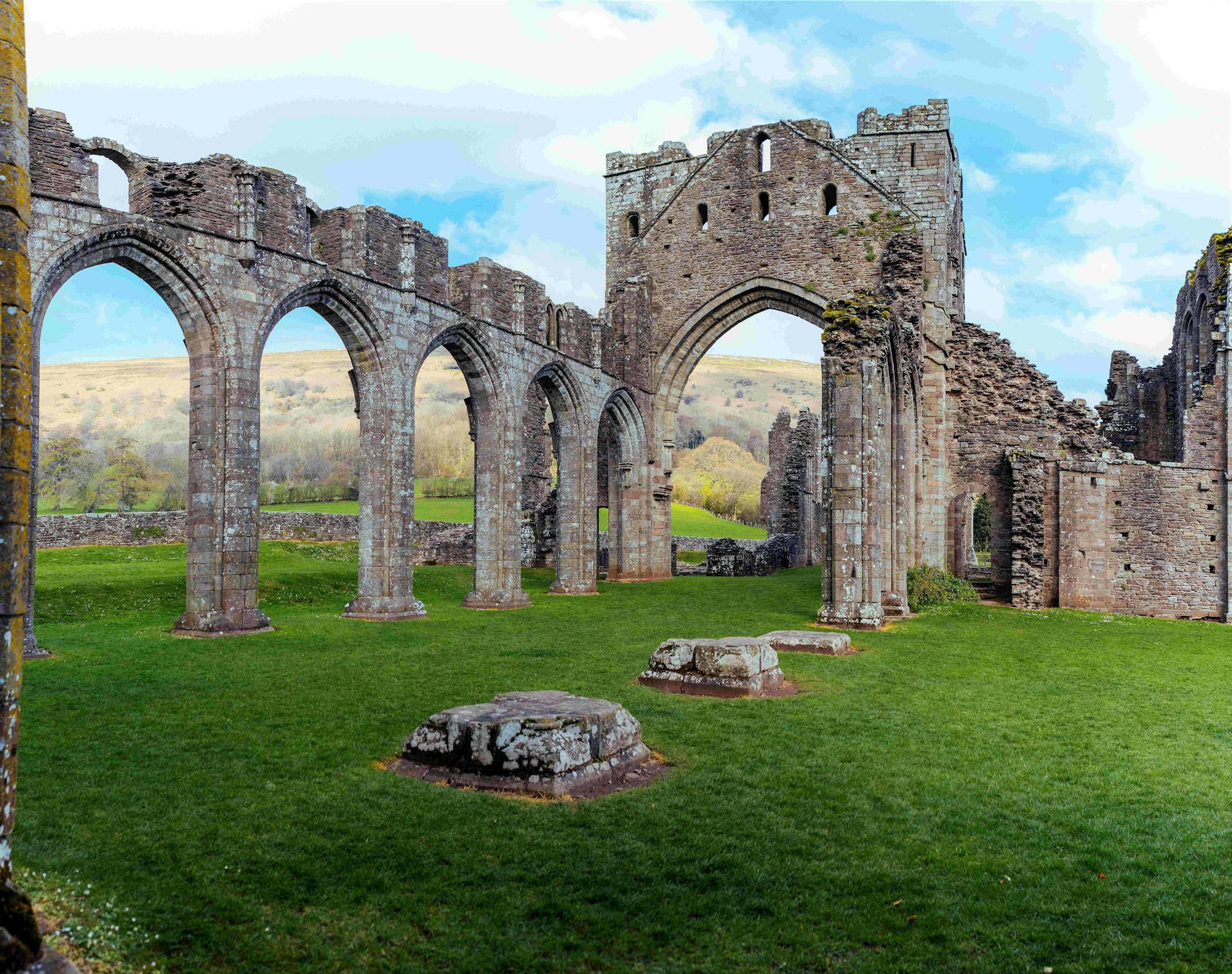 Large stone archways stand in the middle of a green field at the ruins of Llanthony Priory, Wales