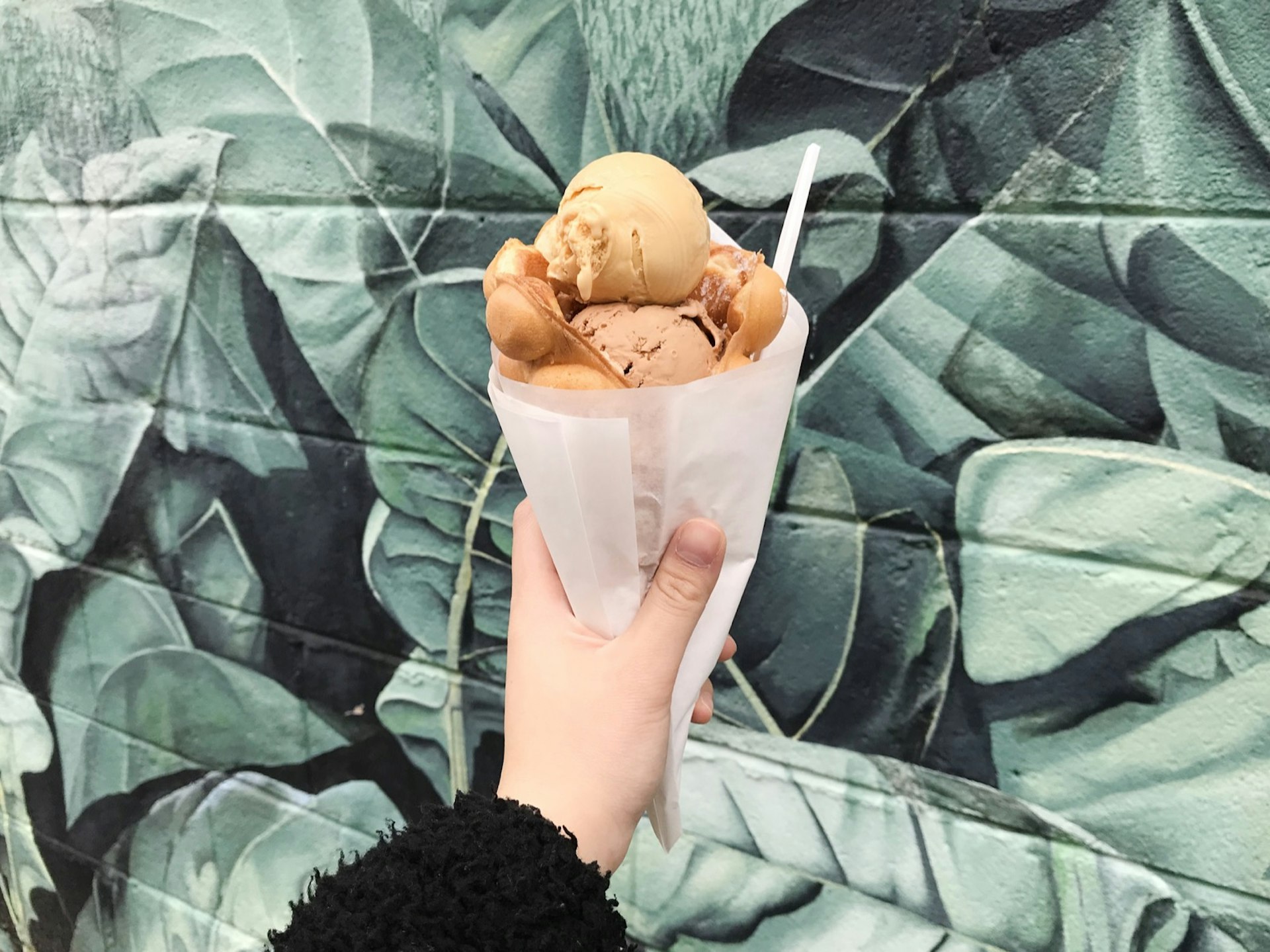 Ice cream is piled high in a rolled up waffle, in front of a mural depicting leaves
