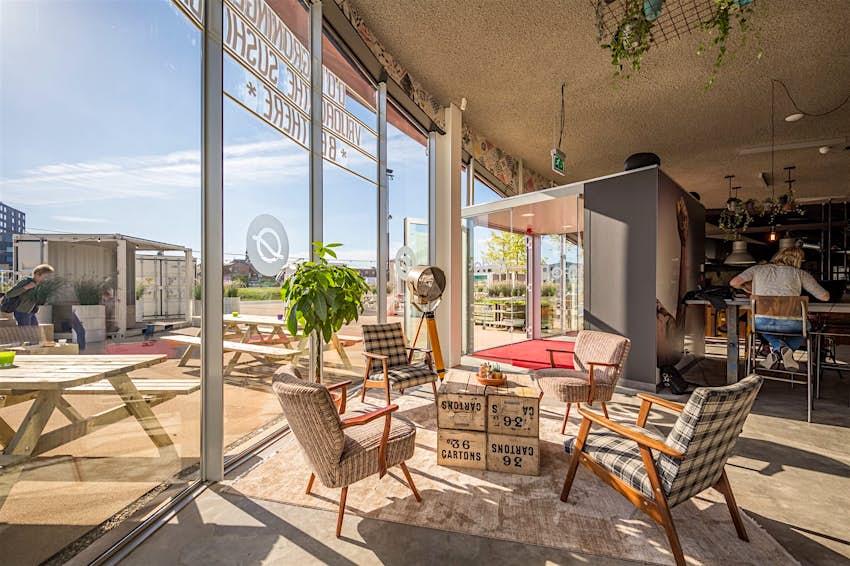 The cafe at DOT Groningen cinema has floor to ceiling windows overlooking blue skies and an urban beach. Comfy chairs surround ramshackle tables indoors, with lots of picnic benches outside. © DOT Groningen