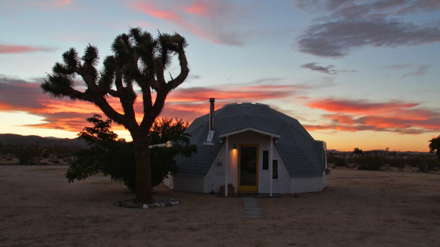 A geo-dome house in a desert next to a Joshua Tree