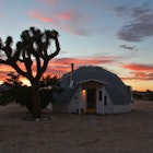 A geo-dome house in a desert next to a Joshua Tree