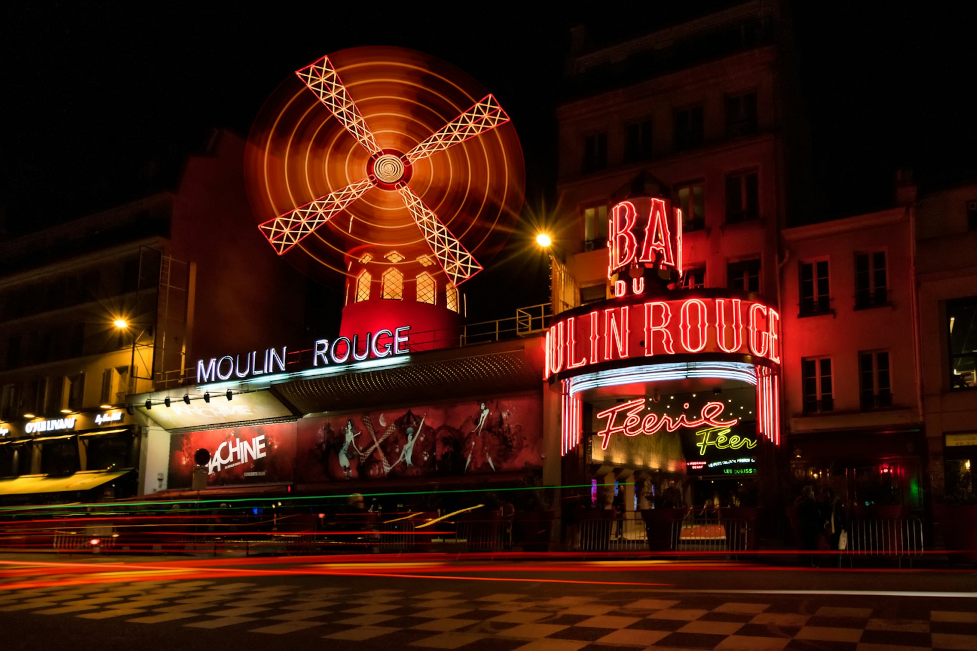 Bathed in red light, the famous windmill in front of the Moulin Rouge cabaret club in Paris spins at night time