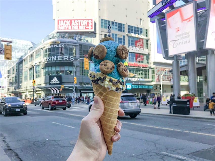 Features - Fugo_Desserts-8febcfa820d6 Full mini chocolate chip cookies are perched on two scoops of blue ice cream in a cone held at a busy intersection