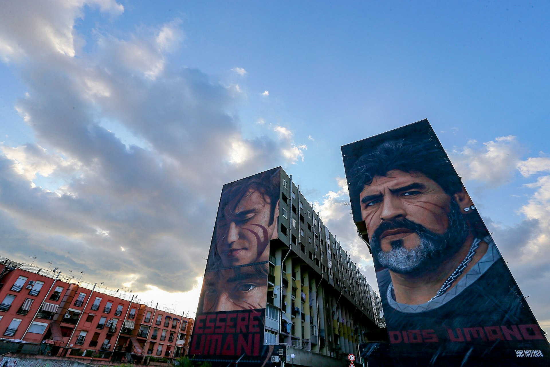 The side of an apartment building is decorated with two huge murals, one of the footballer Maradona's face and the other of a boy's face, both with red face paint on their cheeks