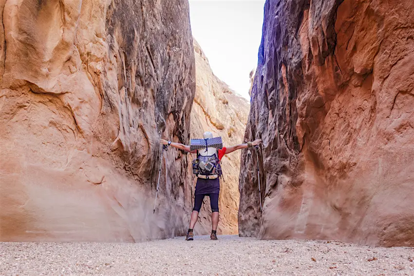 Features - Backpacker in narrow canyon, Hayduke Trail, Utah, USA A backpacker touches both walls in a narrow canyon