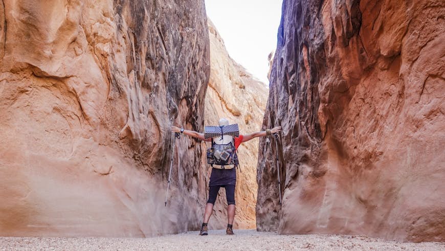 A backpacker touches both walls in a narrow canyon