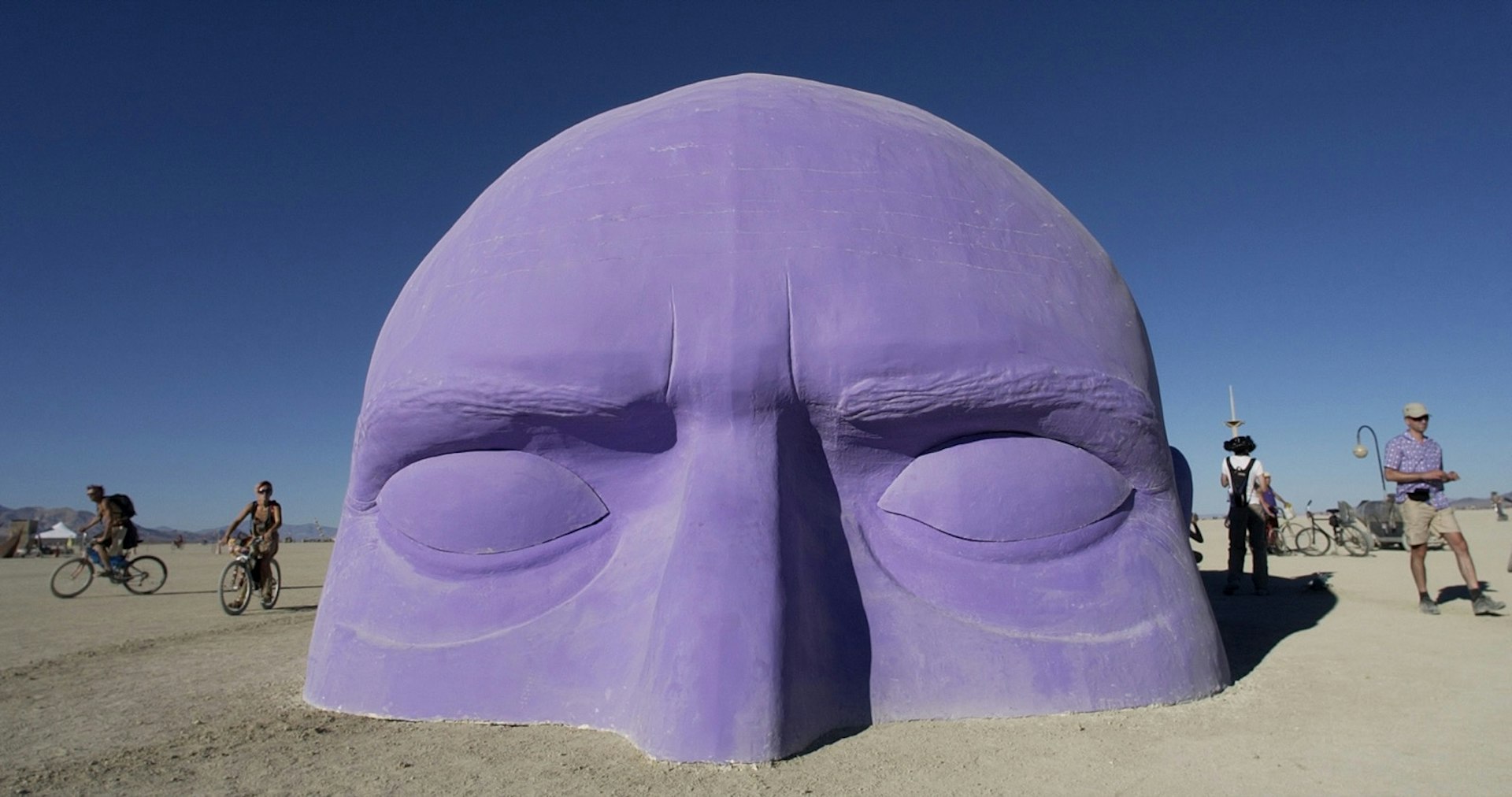 Half of a giant purple head protrudes from the desert