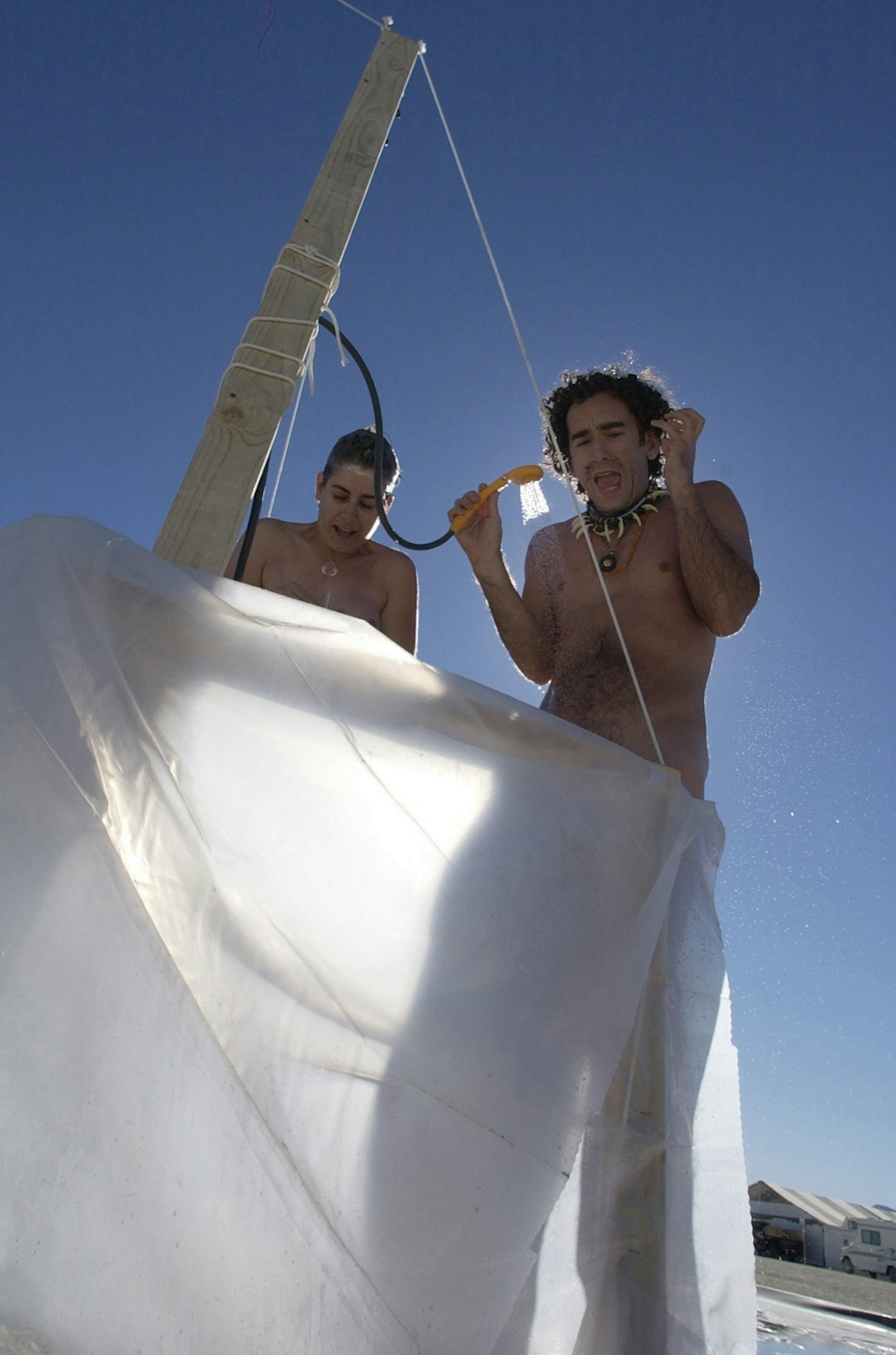 Two people take a shower behind a white sheet, they appear to be cold