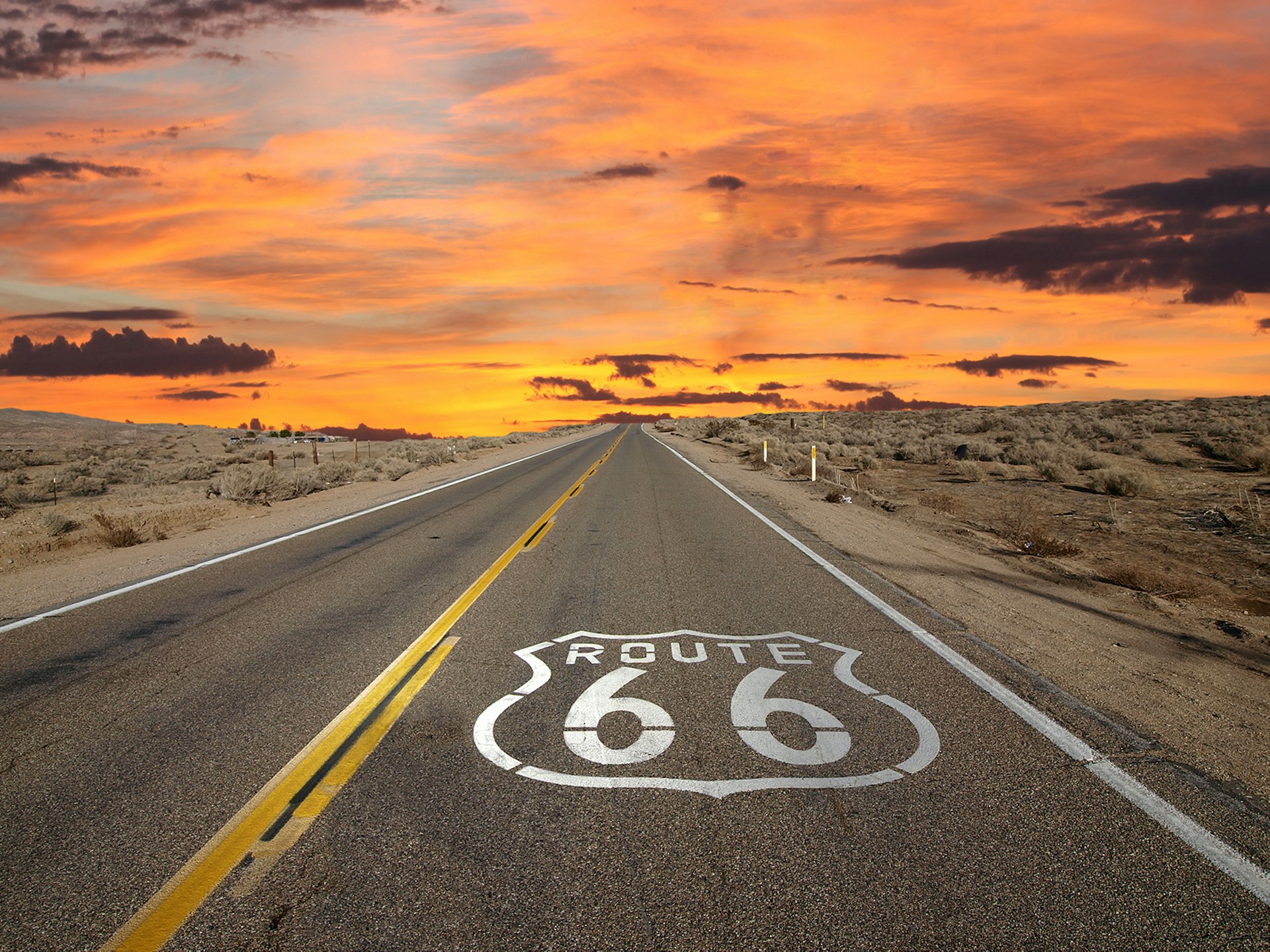 An orange sunset over a road painted with the Route 66 symbol